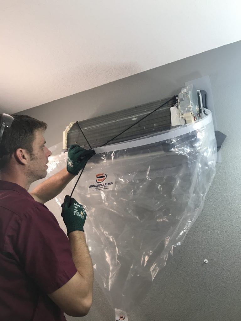 HVAC technician performing professional ductless heat pump cleaning with a SpeedClean bib